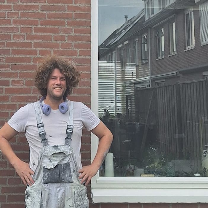 schilder Peter lachend in werkkleding voor een pas geschilderd raam.