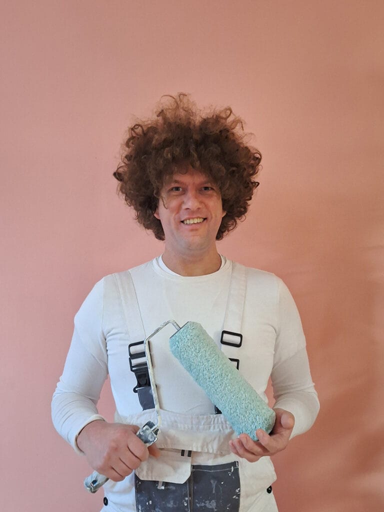 Binnenschilder in utrecht Peter Stoop staat voor een roze muur met een roller in de hand klaar om te helpen.